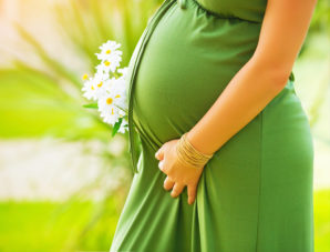 Closeup on tummy of pregnant woman, wearing long green dress, ho